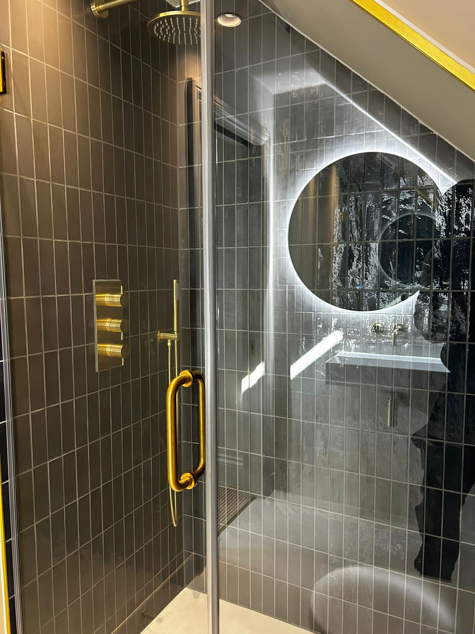 Modern shower installation with dark tiles and gold fixtures